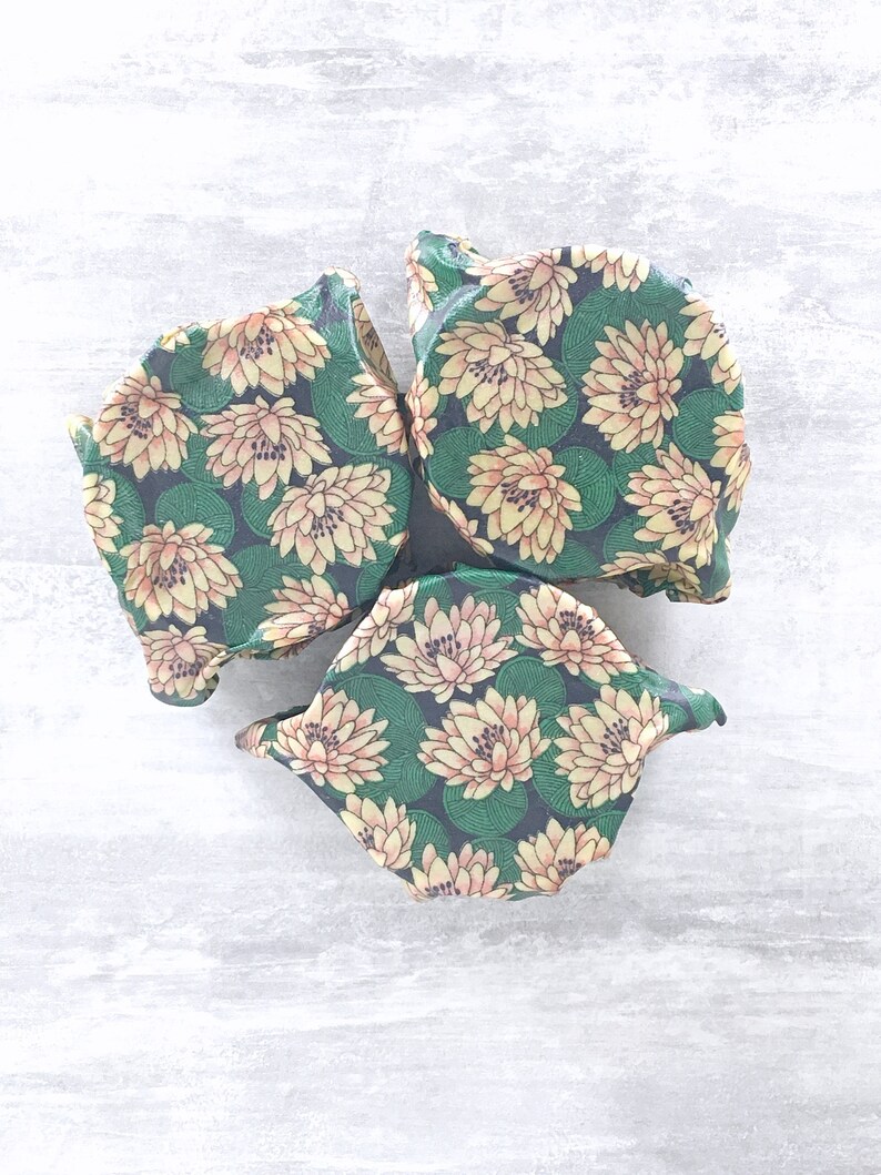 May include: Three reusable food wraps with a floral pattern. The wraps are made of a green and yellow fabric with a floral pattern. The wraps are folded and stacked on top of each other.