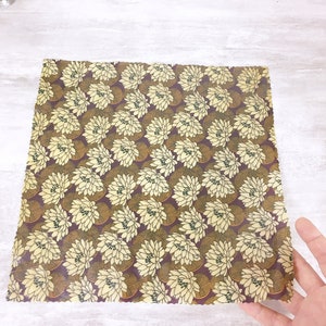 May include: A square piece of beeswax food wrap with a floral pattern. The pattern is yellow and brown on a burgundy background. The wrap is made of natural materials and is reusable and compostable.