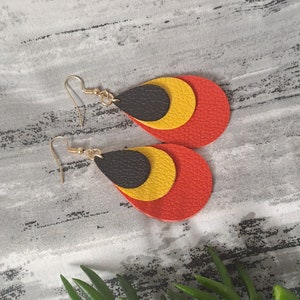 May include: A pair of dangle earrings with three layered teardrop shapes. The top layer is black, the middle layer is yellow, and the bottom layer is red.
