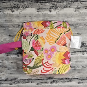 May include: A pink and white drawstring bag with a floral pattern. The bag has a pink strap and a small tag with the text "Handmade with Love".