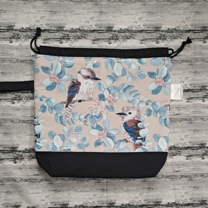 May include: A beige drawstring bag with a black base. The bag features a floral pattern with blue and pink flowers and two blue birds.