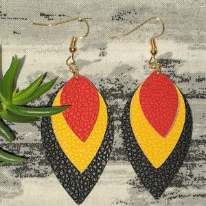 May include: A pair of dangle earrings with three layered leather teardrop shapes. The top layer is red, the middle layer is yellow, and the bottom layer is black.