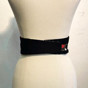 May include: A black obi belt with a red and white floral design. The belt is wrapped around a mannequin. The belt is made of a thick, sturdy material and is designed to cinch the waist.