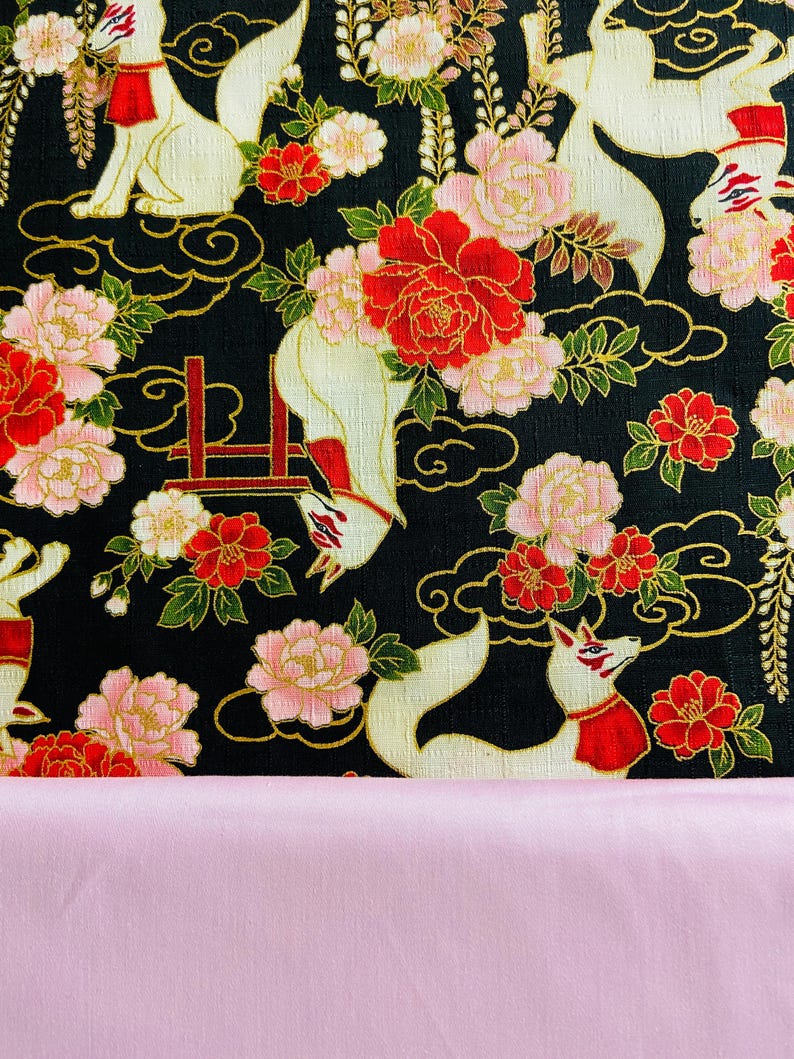 May include: A black fabric with a repeating pattern of white foxes, red and pink flowers, and gold accents. The foxes wear red collars. The bottom of the image shows a solid pink fabric.