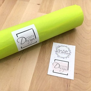 Op de afbeelding: Een rol heldergroen tissuepapier met een wit label waarop "Serena e Grazia Design" staat. Er is ook een aparte witte kaart met een lavendelkrans en de tekst "Una Viola sul Balcone" en een kleiner wit label waarop "Serena e Grazia Design" staat.