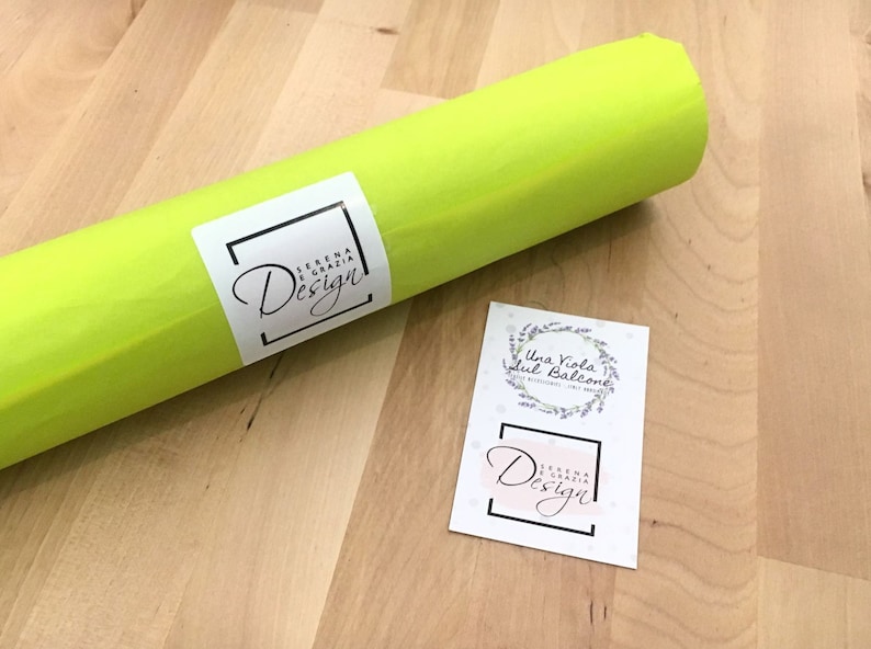 Op de afbeelding: Een rol heldergroen tissuepapier met een wit label waarop "Serena e Grazia Design" staat. Er is ook een aparte witte kaart met een lavendelkrans en de tekst "Una Viola sul Balcone" en een kleiner wit label waarop "Serena e Grazia Design" staat.