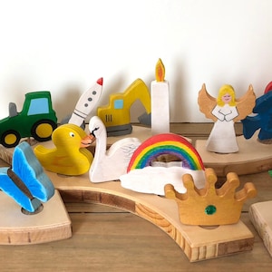 Könnte beinhalten: Ein Holzspielzeugset mit verschiedenen bunten Figuren, darunter ein Dinosaurier, ein Schmetterling, ein Traktor, eine Rakete, ein Bagger, eine Kerze, ein Engel, ein Fisch, ein Herz, ein Mond, eine Tulpe und ein Baum. Die Figuren sind auf einer Holzbasis angeordnet.