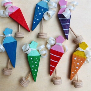 Pode incluir: Um conjunto de dez cones de brinquedo de madeira em várias cores, incluindo azul, verde, rosa, vermelho e amarelo. Cada cone tem um padrão diferente e está preso a uma base de madeira.