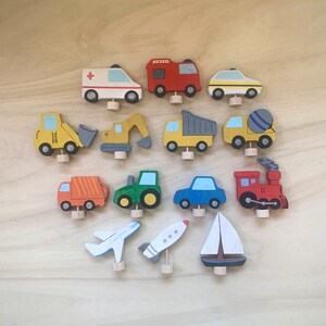 May include: A set of 15 wooden toy vehicles, including a fire truck, ambulance, police car, dump truck, cement mixer, excavator, tractor, airplane, rocket, sailboat, and train. The toys are painted in bright colors and have a whimsical design.