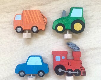 以下が含まれることがあります： 赤い電車、青い車、緑のトラクター、オレンジ色のゴミ収集車の4つの木製のおもちゃの乗り物。各乗り物には、直立させるための小さな木製のダボがあります。
