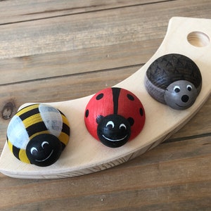 Könnte beinhalten: Holzspielzeug-Set mit drei bemalten Holzfiguren: ein Marienkäfer, eine Biene und ein Igel. Die Figuren befinden sich auf einer Holzbasis.