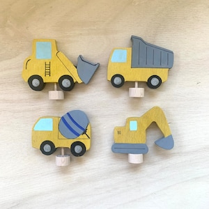 May include: Set of four wooden toy construction vehicles. The vehicles are painted yellow with blue and gray accents. The vehicles include a dump truck, a cement mixer, a bulldozer, and an excavator.