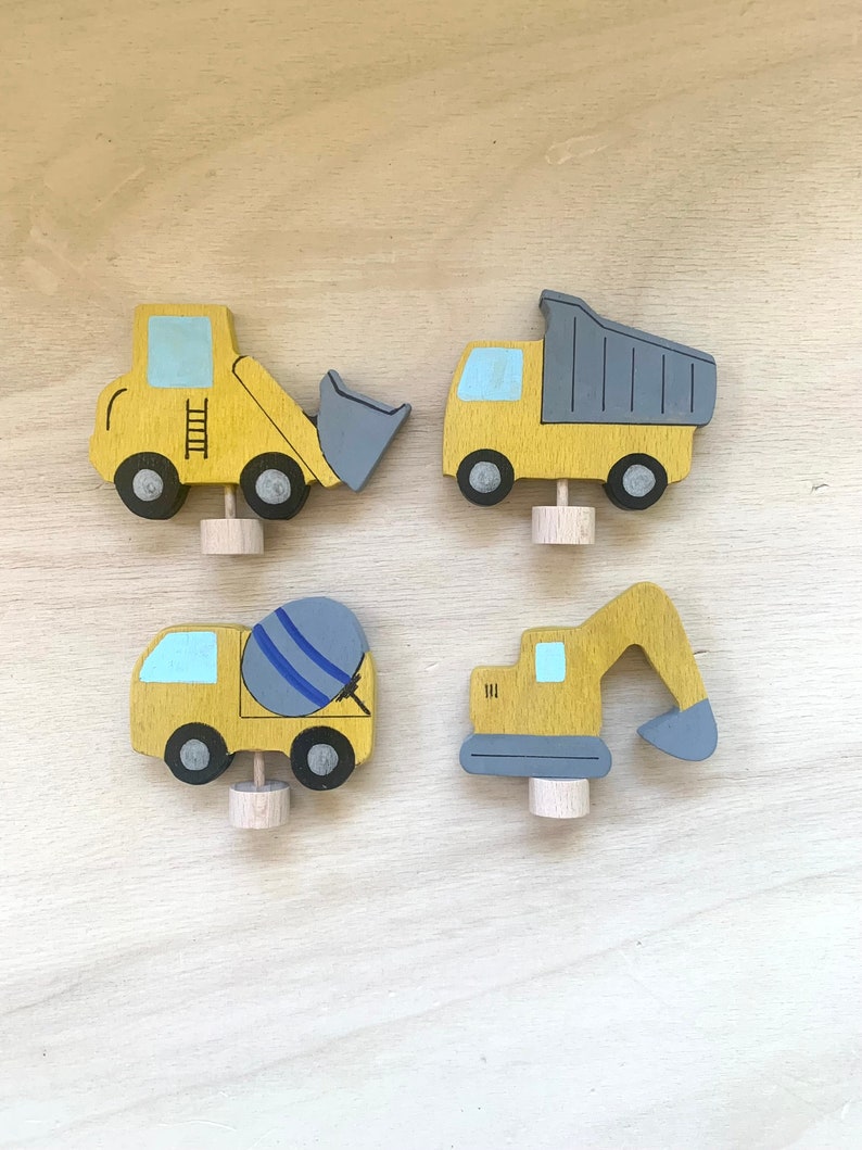 May include: Set of four wooden toy construction vehicles. The vehicles are painted yellow with blue and gray accents. The vehicles include a dump truck, a cement mixer, a bulldozer, and an excavator.