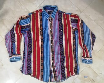 Puede incluir: Una camisa abotonada de manga larga con un colorido estampado de rayas. La camisa presenta rayas verticales en rojo, azul y morado, con diseños de cachemira y geométricos. El cuello y los puños son azules, y la camisa tiene una etiqueta Wrangler.