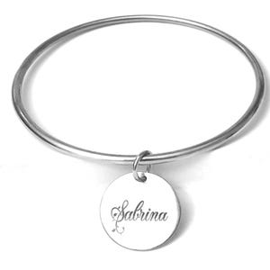 Peut inclure: Un bracelet jonc argenté avec un charm circulaire. Le charm est gravé du nom "Sabrina" en écriture cursive. Le bracelet est de conception simple et élégante.