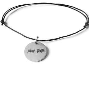 Può includere: Una collana con cordoncino nero e un ciondolo rotondo in argento che dice "MON TEXTE" in un font stilizzato.