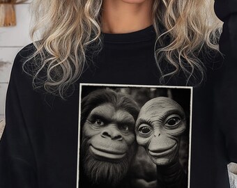 May include: Black sweatshirt featuring a square, black and white image of two smiling, cartoon-like creatures. The sweatshirt has a crew neck and long sleeves. The word "Black" is printed in the bottom right corner.