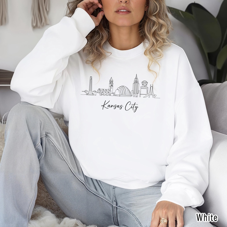 May include: A white ceramic mug with a black handle and the text "But First, Coffee" in a bold, black font. The mug is set against a blurred background, suggesting a cozy setting.