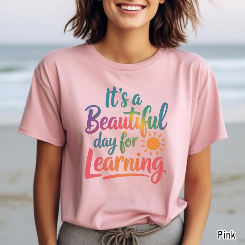 May include: Pink t-shirt with the text "It's a Beautiful day for Learning" in a rainbow gradient font. A yellow and orange sun graphic is included. The shirt is short-sleeved.