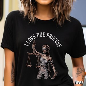 May include: Black t-shirt featuring a graphic of Lady Justice holding scales, with the text "I LOVE DUE PROCESS" in white. The design is centered on the shirt, with the word "Black" in the bottom right corner.