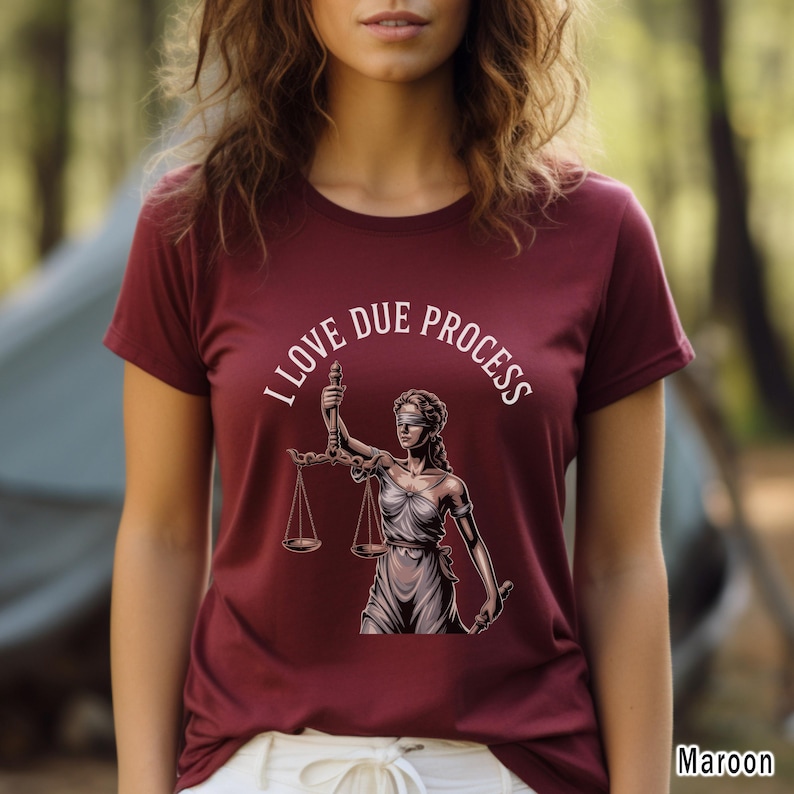 May include: Maroon t-shirt with the text "I LOVE DUE PROCESS" and an illustration of Lady Justice holding scales. The design features a blindfolded woman in a toga, symbolizing justice. The shirt is a solid maroon color.