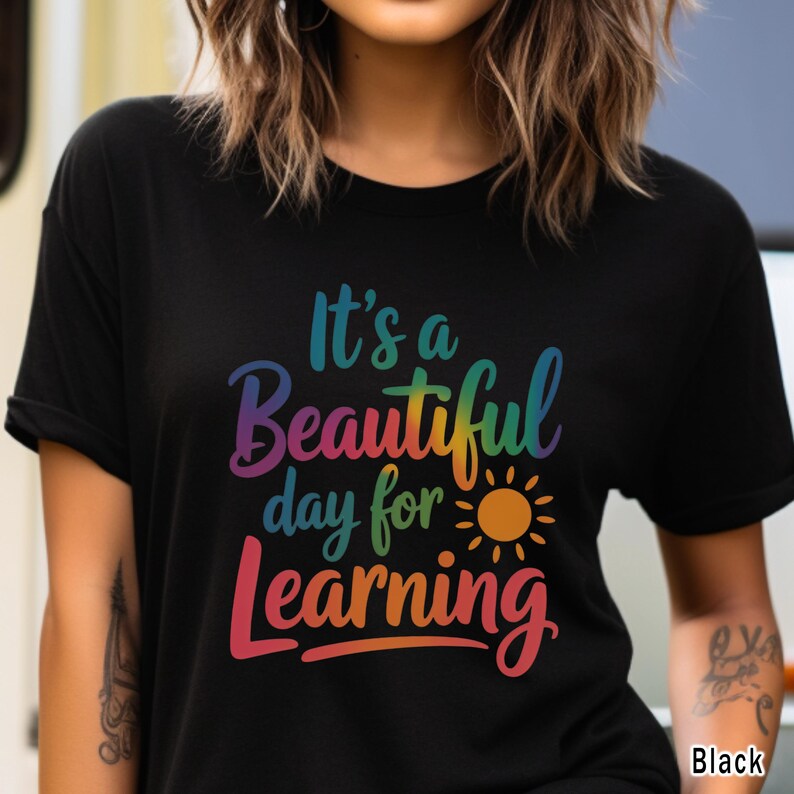 May include: Black t-shirt with the text "It's a Beautiful day for Learning" in a rainbow gradient. A yellow and orange sun graphic is included. The shirt is a crew neck style.
