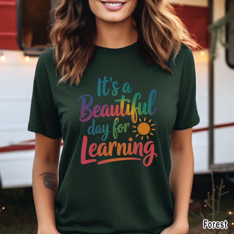May include: Dark green t-shirt with the text "It's a Beautiful day for Learning" in rainbow colors, with a yellow sun graphic. The shirt is a short-sleeved crew neck.