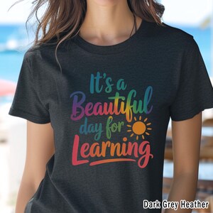 May include: Dark grey heather t-shirt with the text "It's a Beautiful day for Learning" in rainbow colors. A yellow sun graphic is included in the design. The shirt is a crew neck style.