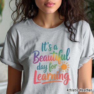 May include: A heather gray t-shirt with the text "It's a Beautiful day for Learning" in colorful script. The design includes a sun graphic. The shirt is labeled "Athletic Heather".