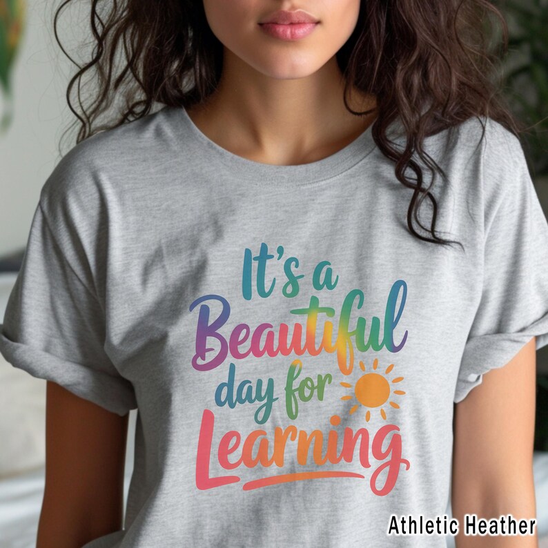 May include: A heather gray t-shirt with the text "It's a Beautiful day for Learning" in colorful script. The design includes a sun graphic. The shirt is labeled "Athletic Heather".