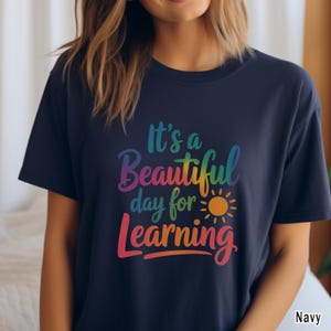 May include: Navy blue t-shirt with the text "It's a Beautiful day for Learning" in rainbow colors. The design includes a sun graphic. The shirt is a casual wear item.