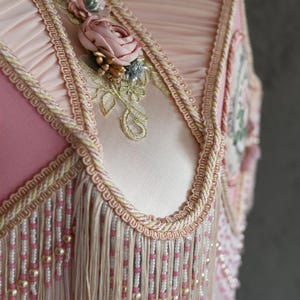 Pu&ograve; includere: Un paralume rosa con una frangia di perline e ricami floreali. Il paralume ha un bordo a festoni e un delicato motivo floreale.