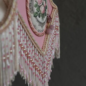 Pu&ograve; includere: Un paralume rosa con un motivo floreale e una frangia di perline. Il motivo floreale presenta rose e la parola "Victoria" &egrave; stampata sul paralume.