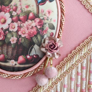 Pu&ograve; includere: Un paralume rosa con un pannello rotondo in tessuto con motivo floreale che presenta un uccello, ciliegie e fragole. Il pannello &egrave; circondato da una treccia marrone e una frangia bianca e dorata.