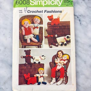 Può includere: Una busta per cartamodello vintage Simplicity 6008 per moda all'uncinetto. La copertina presenta illustrazioni di bambole e animali di peluche fatti a mano, tra cui un gatto, un orso, un cane e due bambole, con il testo 6008 Simplicity.