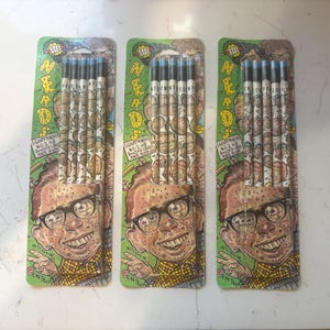 May include: Three packages of pencils with a cartoon image of a nerdy man with glasses. Each package contains five pencils with blue erasers and a repeating pattern of the same cartoon face. The packaging is green and has the words "GOOFY PENCILS" printed on it.