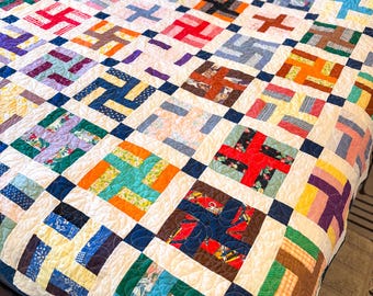 Könnte beinhalten: Eine handgefertigte Steppdecke mit Patchwork-Design. Die Steppdecke weist ein sich wiederholendes Muster aus farbenfrohen Blöcken in verschiedenen Blau-, Grün-, Orange-, Rot- und Gelbtönen auf, die vor einem weißen Hintergrund angeordnet sind. Die Steppdecke liegt auf einem Bett.