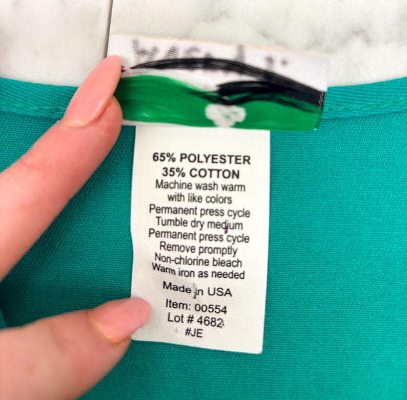 May include: A close-up of a teal fabric with a white tag attached. The tag lists the fabric composition as 65% polyester and 35% cotton, along with washing instructions. The tag also includes the text "Made in USA", item and lot numbers.