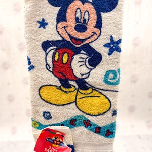May include: White Mickey Mouse 2-piece bath set. The towel features a large image of Mickey Mouse in his classic outfit, with blue stars and a blue and turquoise border. The set includes a matching washcloth.
