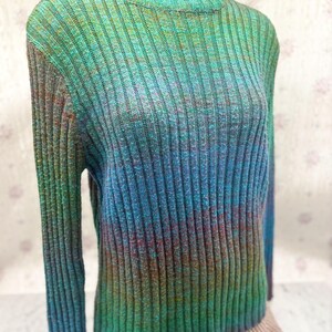 May include: A ribbed knit turtleneck sweater in a gradient of colors, transitioning from green to blue and purple. The long-sleeved sweater has a high neckline and a fitted silhouette, suitable for cooler weather.