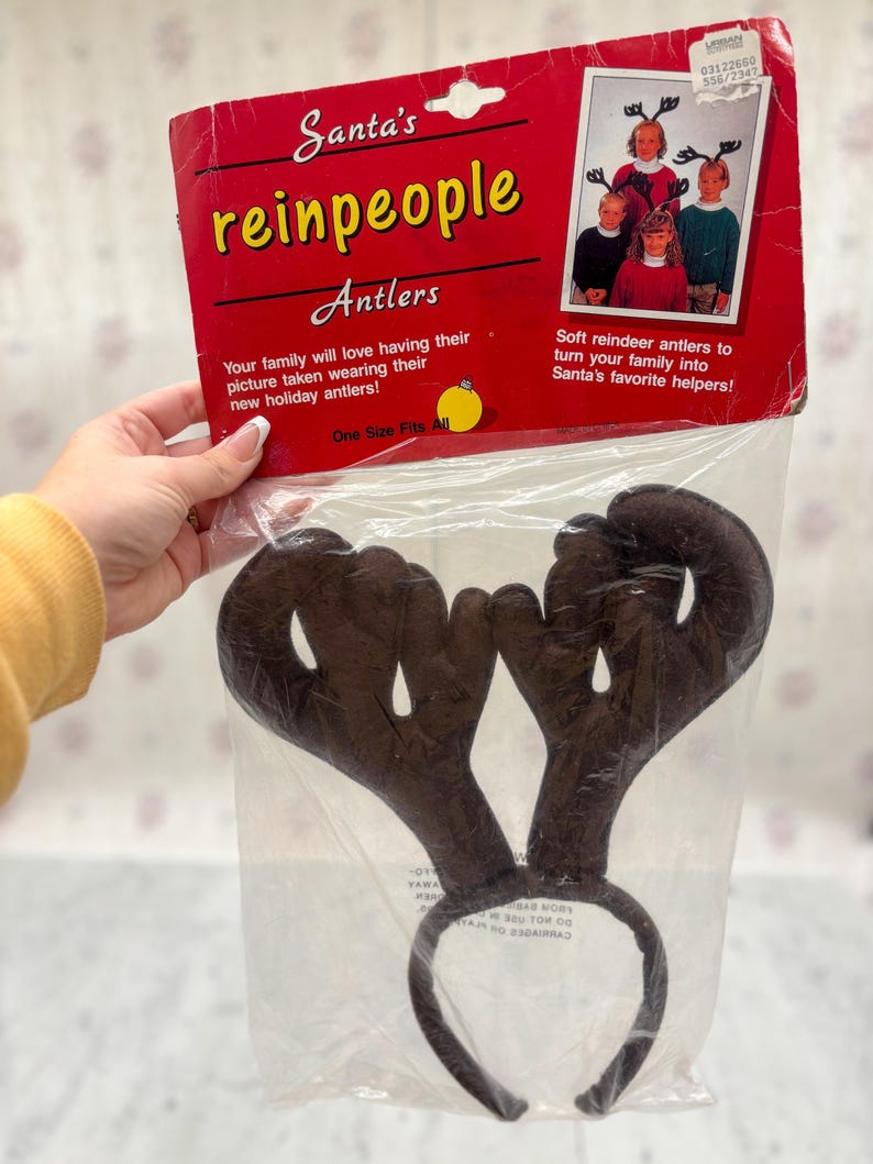 May include: Brown reindeer antler headband in a clear plastic package. The package is red and has the text "Santa's reinpeople Antlers". The text on the package says "One Size Fits All".