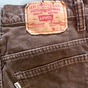 Puede incluir: Primer plano de pantalones de pana marrones con una etiqueta de Levi's. La etiqueta dice "LEVI STRAUSS & CO. ORIGINAL RIVETED CLOTHING" e incluye el logotipo de Levi's. Los pantalones son talla W30 L34.