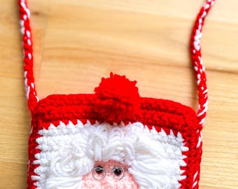 May include: A handmade, red and white crocheted Santa Claus purse with a matching strap. The purse features a Santa face with white beard, pink face, and small wire-rimmed glasses. A red pom-pom adorns the top.