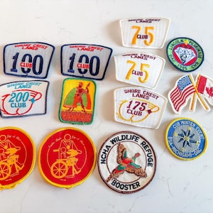 May include: A collection of vintage embroidered patches with various designs. Patches include bowling lane logos, Hawaiian scenes, flags, and wildlife imagery. The patches feature text like "100 Club", "75 Club", and "NCHA Wildlife Refuge".