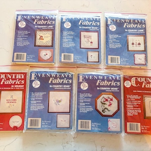 May include: Seven Evenweave and Country Fabrics cross-stitch kits in plastic packaging. The kits feature various designs, including floral patterns and holiday themes. The packaging includes the text "Welcome Friends".