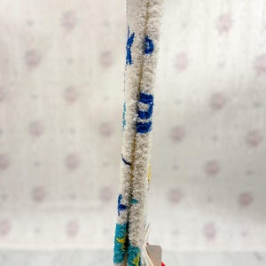 May include: White, fluffy socks with blue and yellow accents. The socks have a textured appearance and feature a pattern of blue letters and shapes. A red tag is attached to the socks.