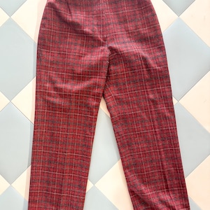 May include: Red plaid trousers with a straight leg. The pants feature a button closure and a classic plaid pattern in red, black, and a hint of gold. The fabric appears to be a woven material.