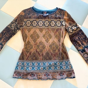 May include: A long-sleeve top featuring a brown and tan damask pattern across the chest, accented by horizontal bands of blue and brown floral motifs. The garment has a round neckline and a lettuce-edge hem, crafted from a semi-sheer fabric.