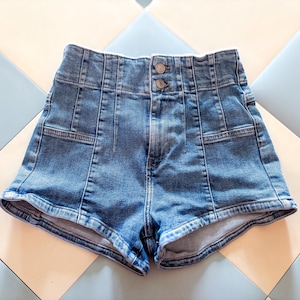 May include: High-waisted blue denim shorts with a button closure. The shorts feature a classic five-pocket design and a tailored fit. The denim has a medium wash and visible stitching details.