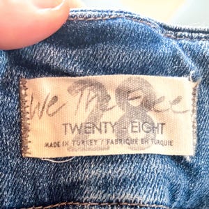 May include: Close-up of a denim garment with a label that reads "We The Free Twenty Eight." The label is stitched onto the blue fabric. The text "Made in Turkey / Fabriqu&eacute; en Turquie" is also visible.